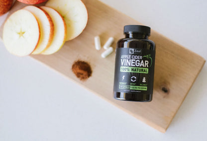 Apple Cider Vinegar capsules on top of a cutting board next to sliced apples, some acv capsules and  pepper. 