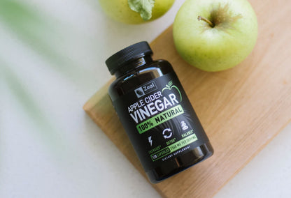 Bottle of apple cider vinegar on cutting board next to a whole apple